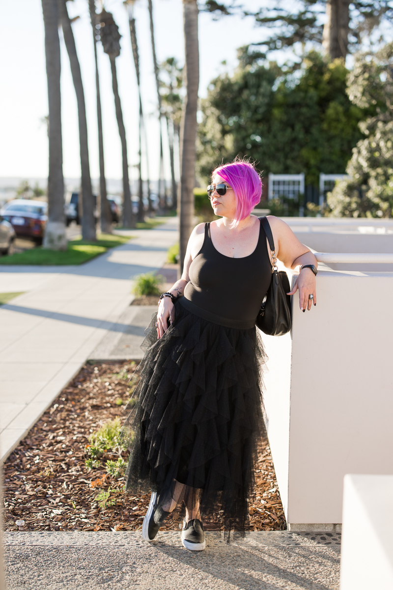 Woman wearing a black top and black skirt posing in the San Diego streets looking off-camera. 
