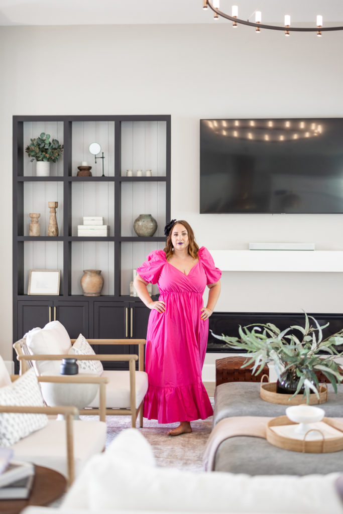Woman wearing a bright pink dress, standing in a living room and looking fiercely toward the Meg Marie camera. 
