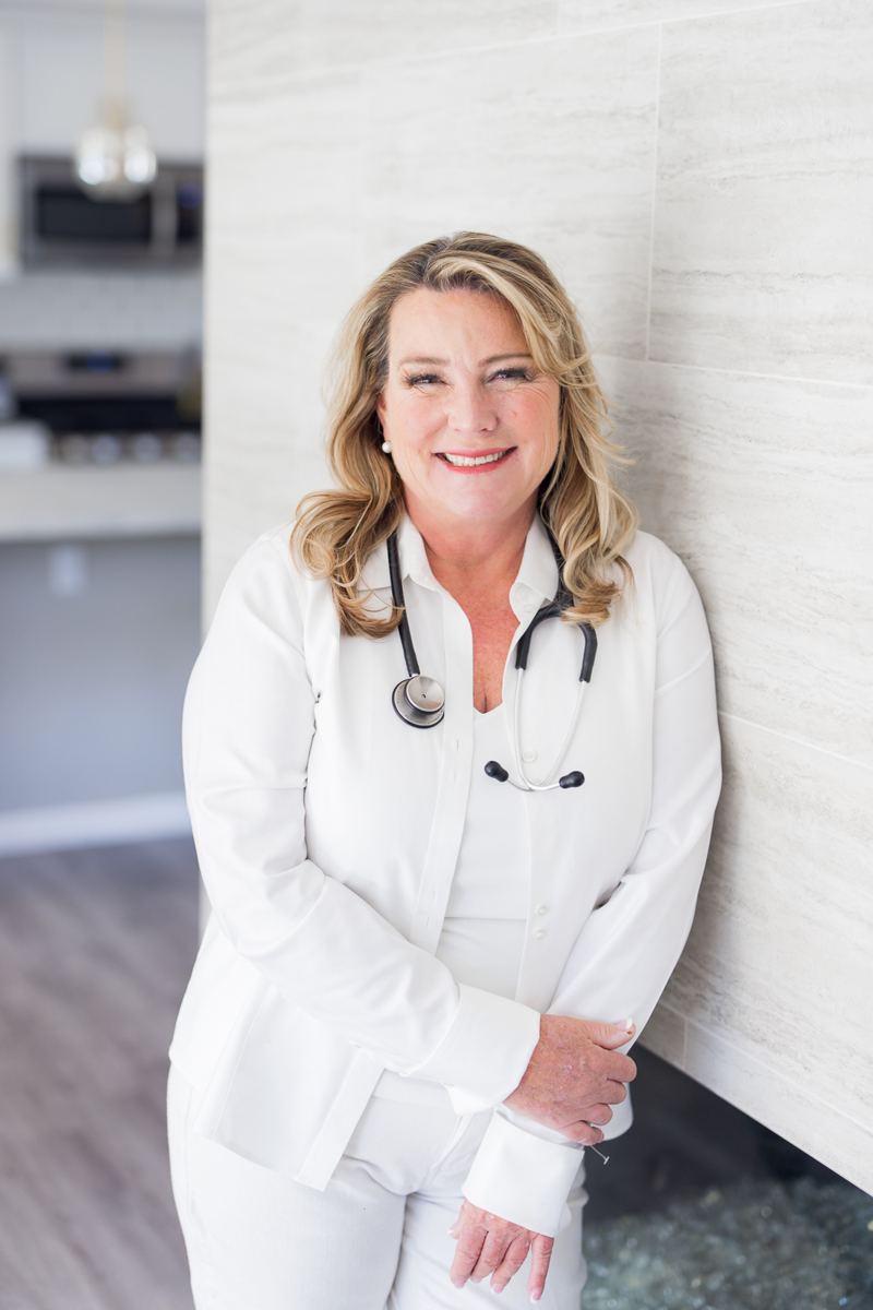 Woman wearing all white with a stethoscope around her neck, smiling at the camera during her branding photoshoot. 

