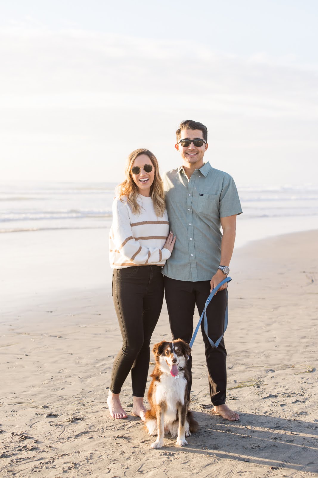 Kellen, hubby, and their dog smiling at the camera during their Meg Marie photography session on the beach. 