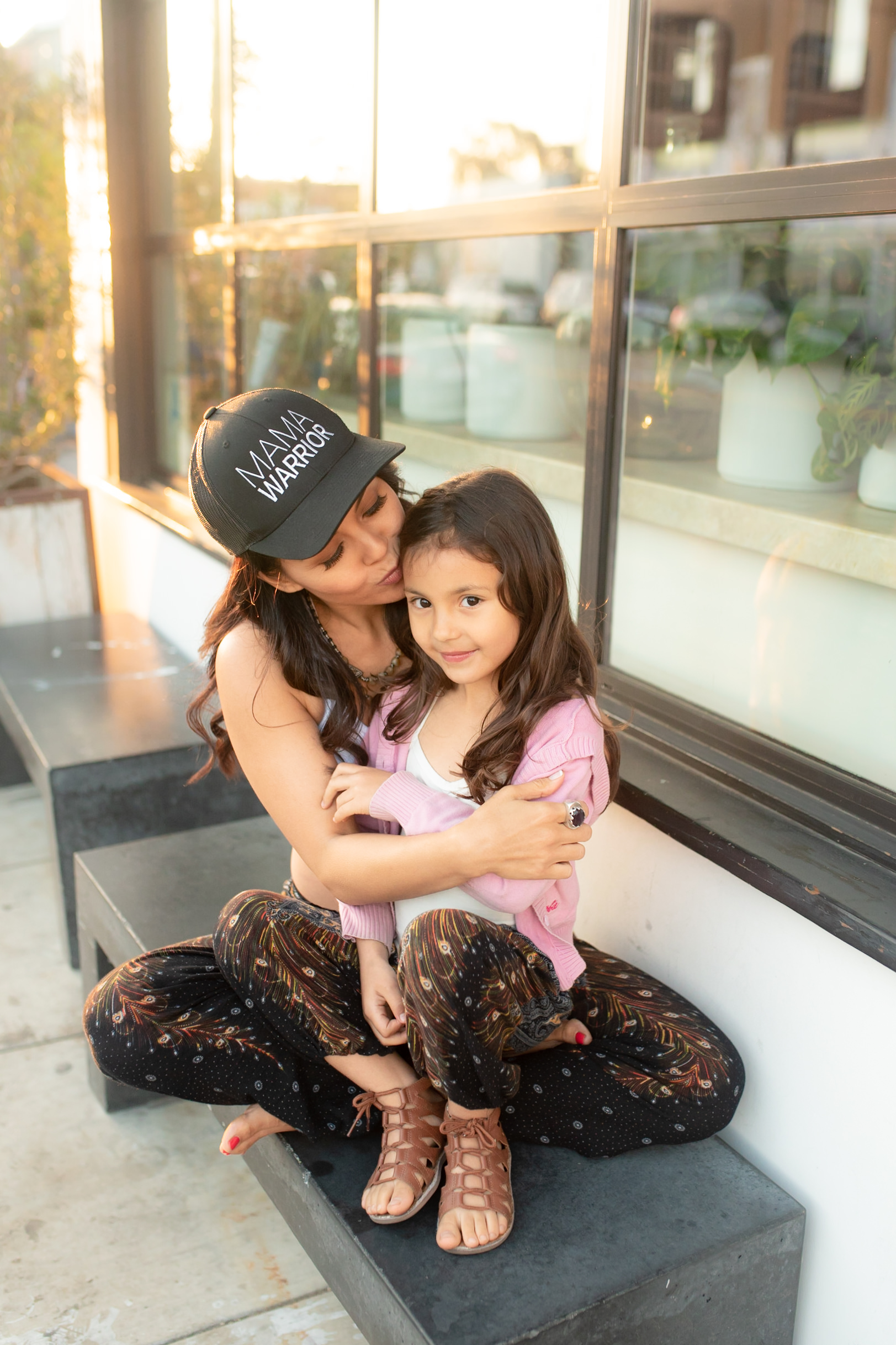  Mompreneur and manifestation coach Xandrine Ayla sitting on a bench with her daughter in her lap and giving her a kiss. 
