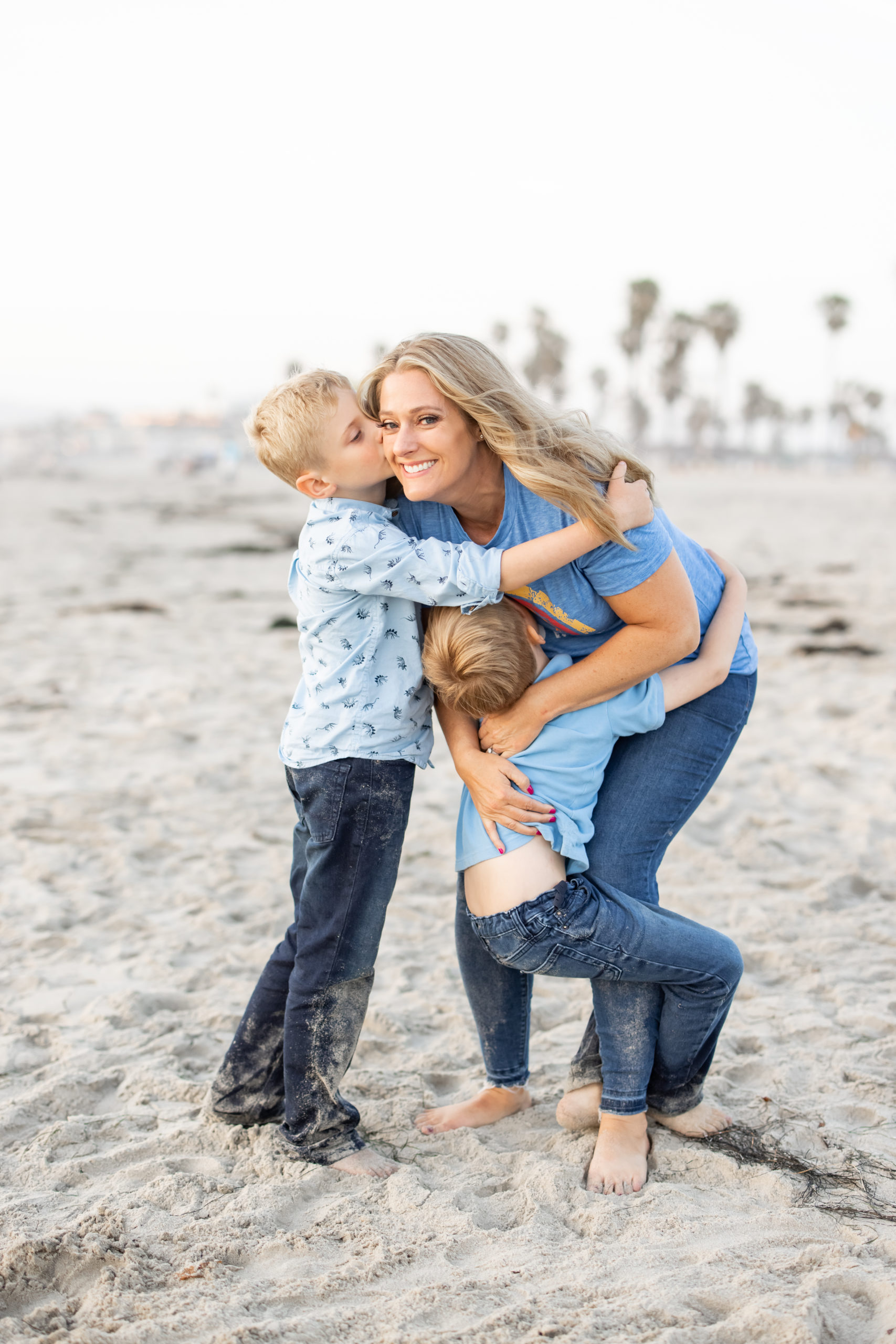 Julie Boyadjian hugging her two boys at the San Diego beach and smiling at the camera.