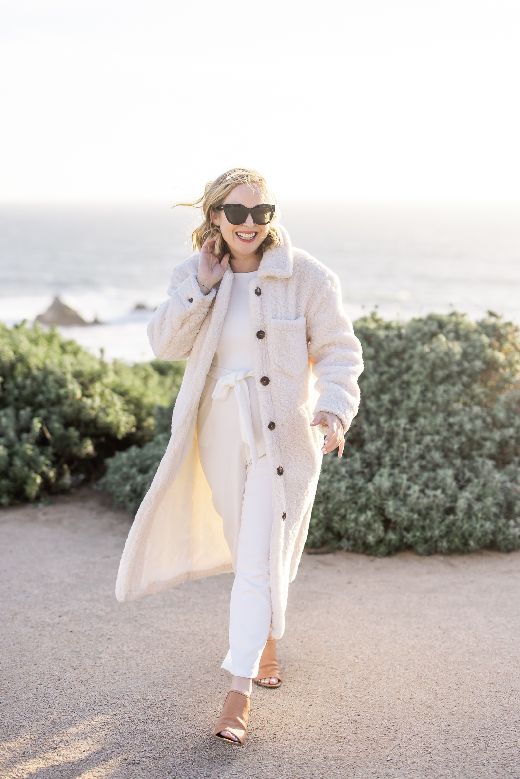 Woman dressed in a white winter coat, walking toward the brand photographer and smiling. 
