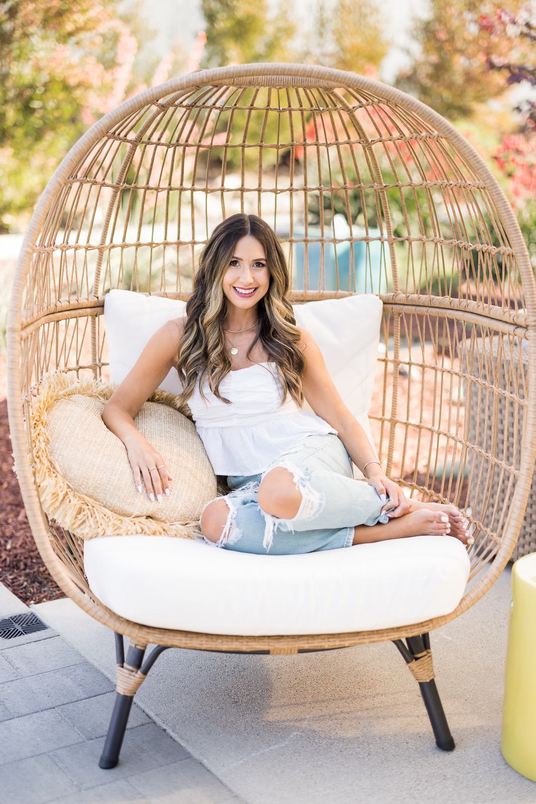 Woman sitting outside on a big chair with jeans and a white shirt, smiling at the camera. 