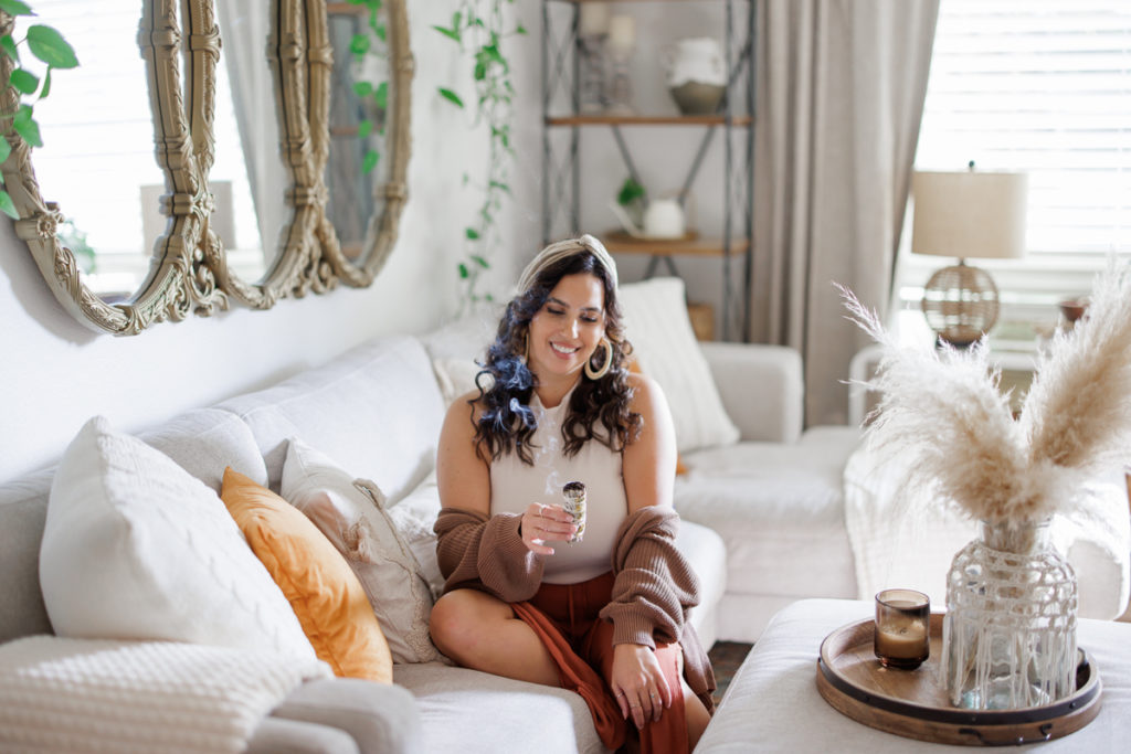 Woman sitting on the couch with a drink in hand and smiling during her personal branding photography shoot. 
