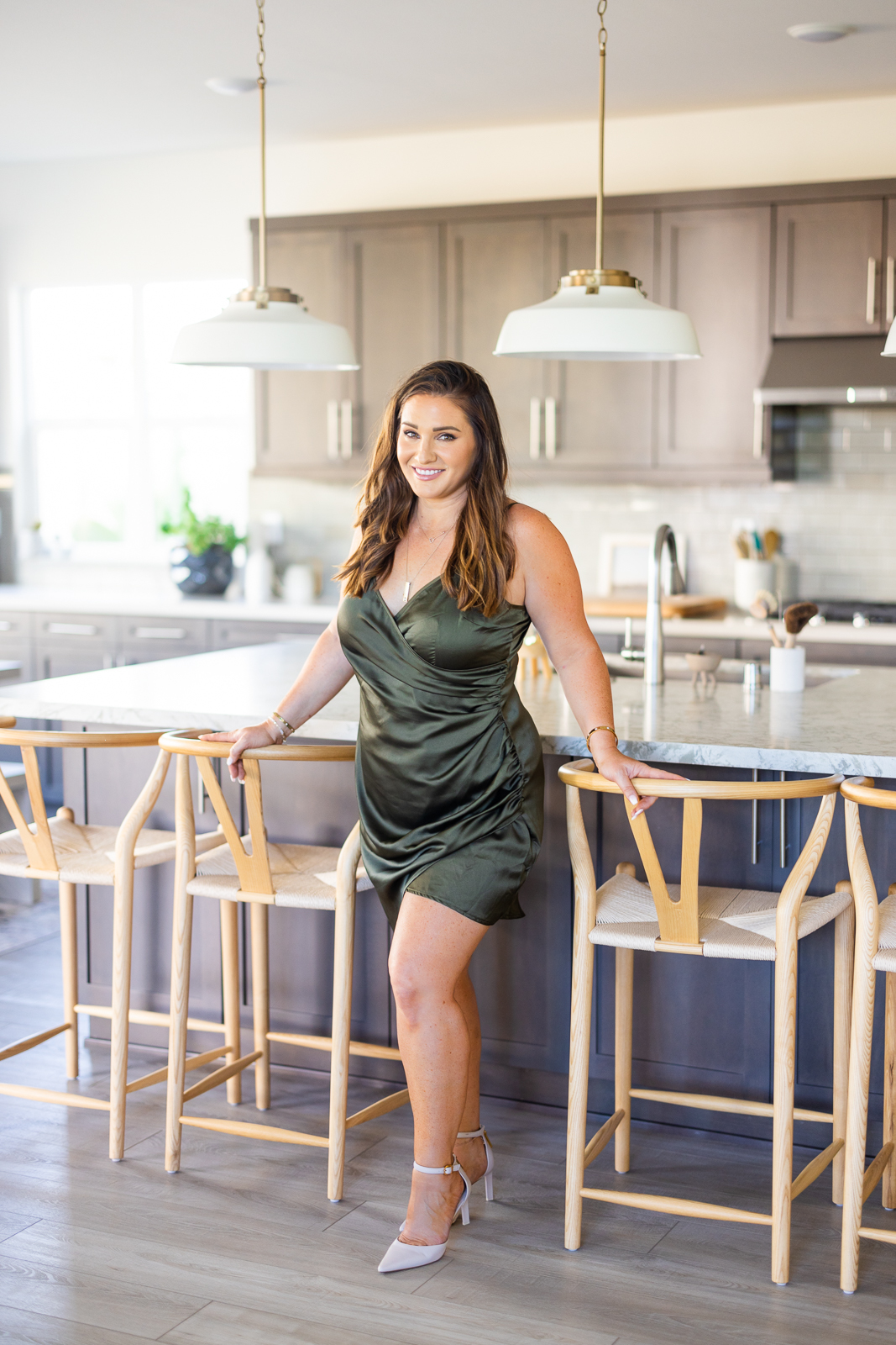 Woman standing next to the bar stools in a kitchen, smiling toward the camera and Meg Marie.