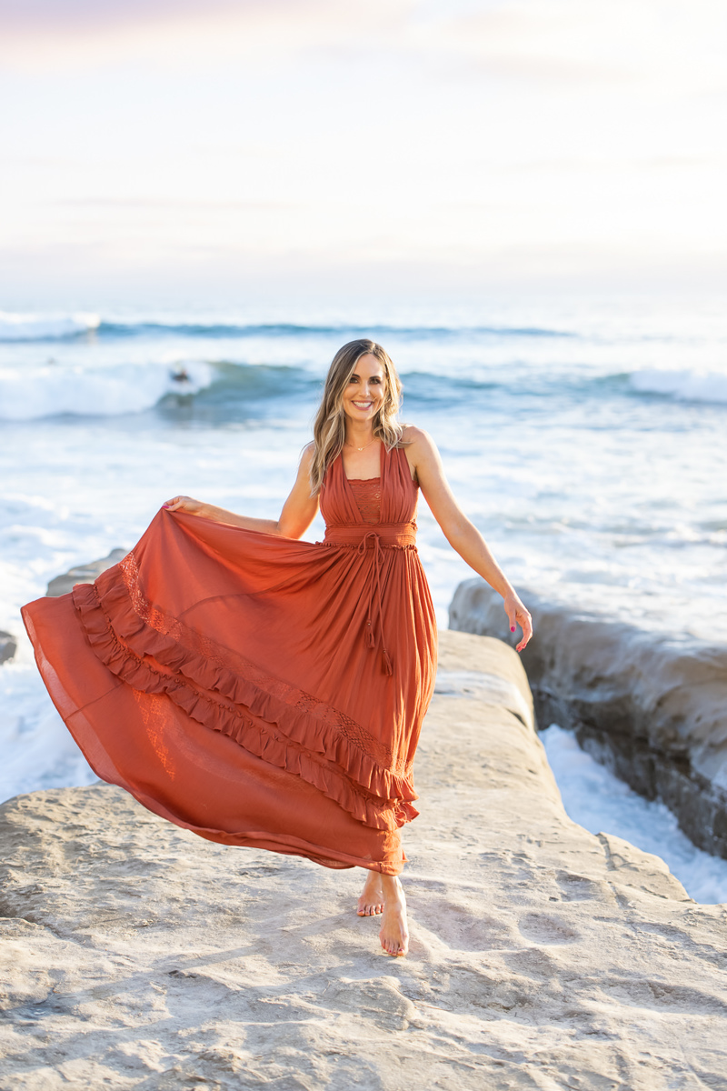 Woman in a dress walking on rocks at the beach, smiling at Meg Marie, the brand photographer.