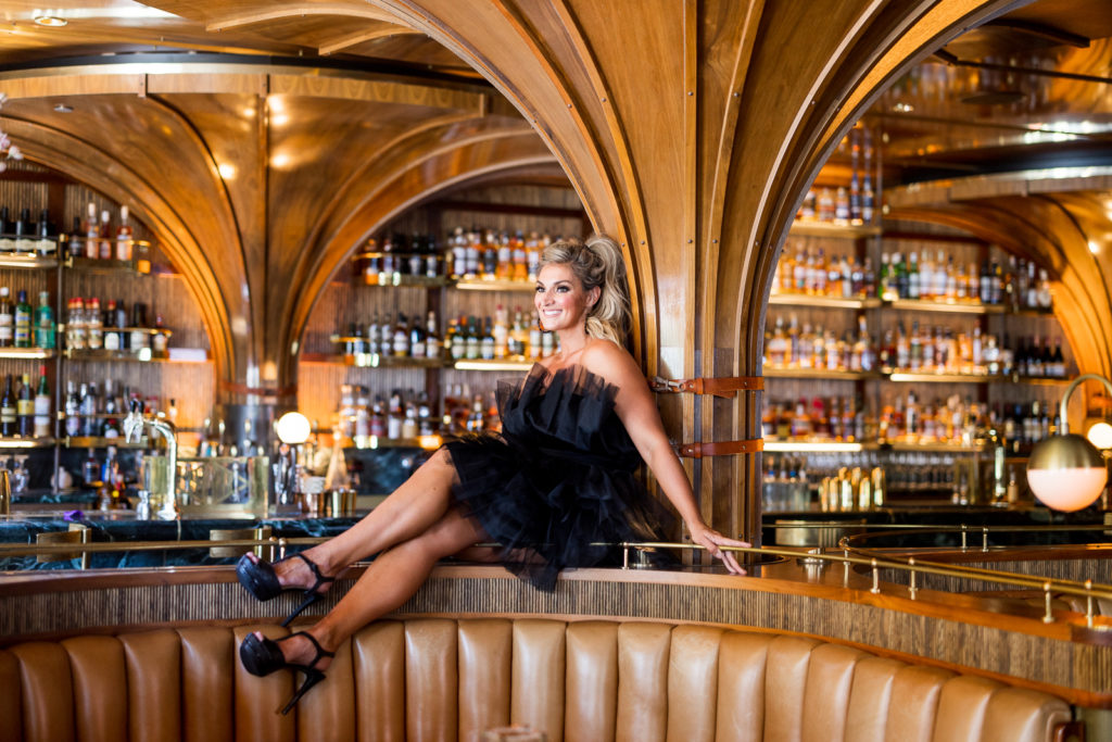 Woman sitting on top of a table at Born and Raised in San Diego wearing a black tulle dress and heels. 
