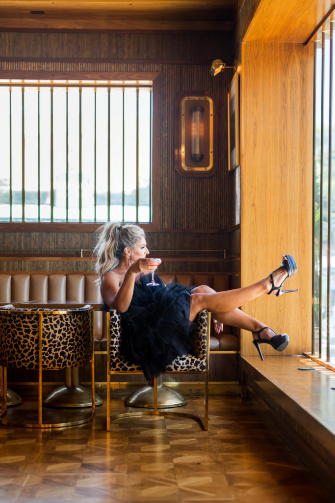 Woman sitting on a chair at a San Diego bar holding a drink, looking away from Meg Marie during her photo shoot. 