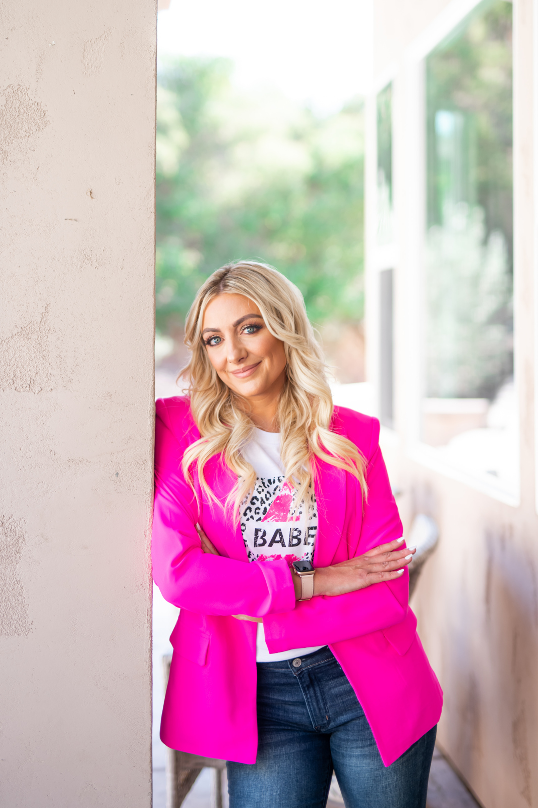Woman wearing a pink jacket, standing in between two walls smiling for the camera. 
