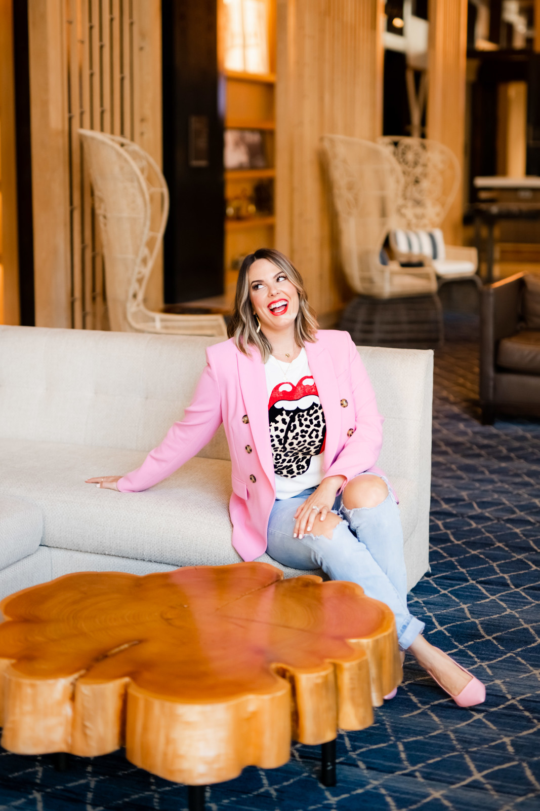 Woman wearing a pink jacket sitting in a lounge area, looking away from the camera and smiling.
