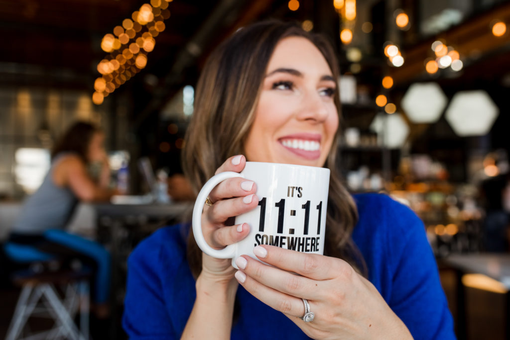 Woman smiling and holding a mug that says it’s 11:11 somewhere.
