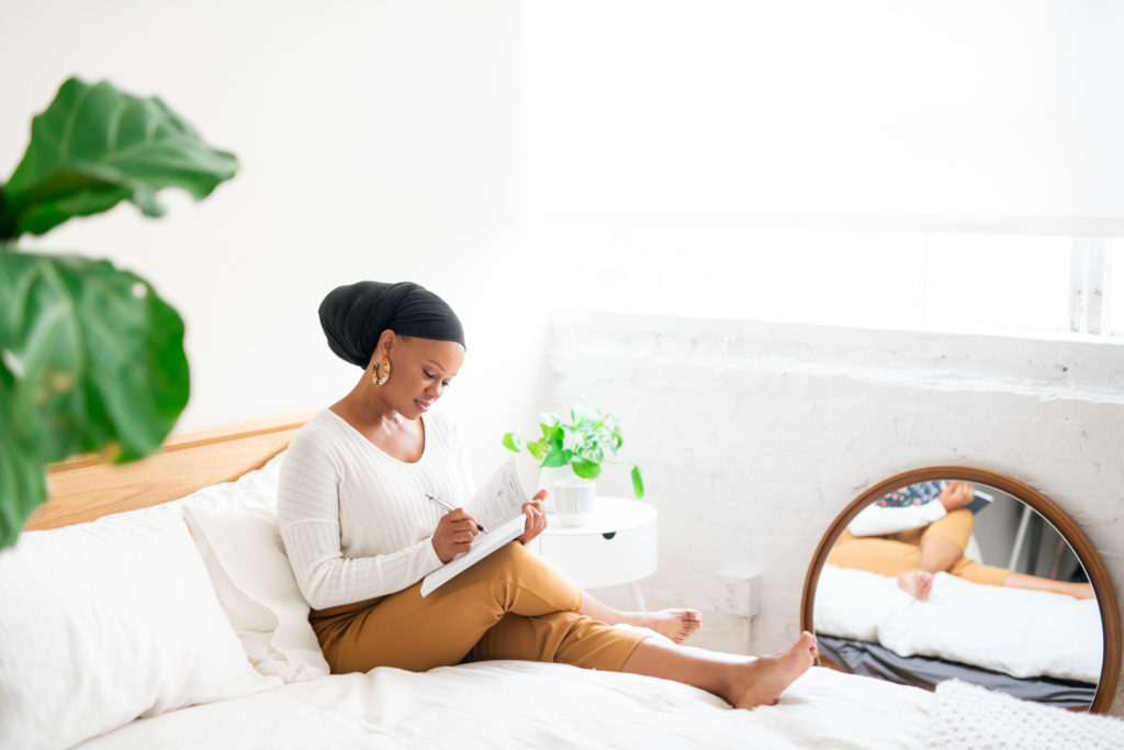 Woman journaling in bed on top of a white comforter. 
