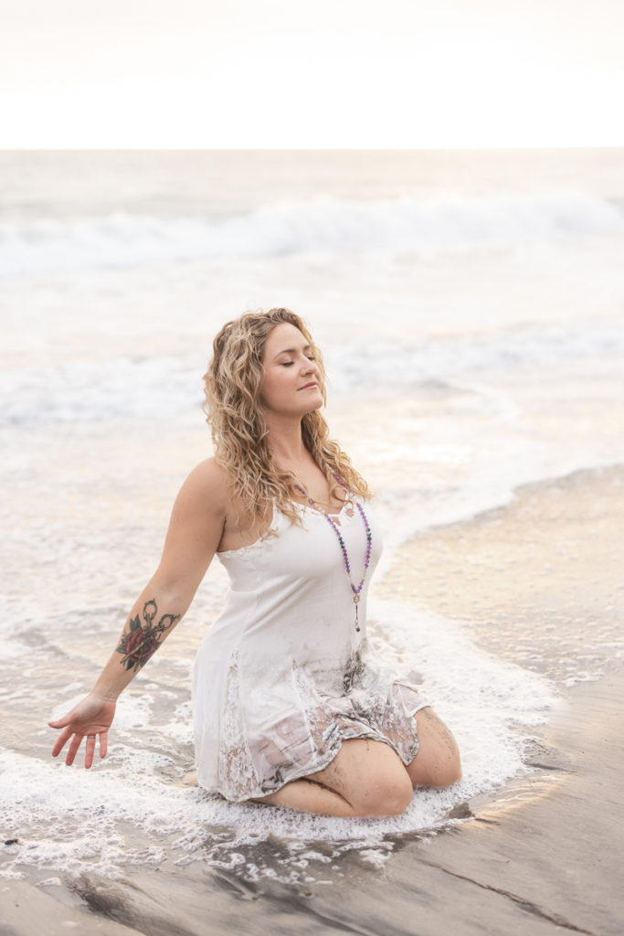 Spiritual entrepreneur doing a mindset ritual in the water at the beach while wearing a mala bead necklace.
