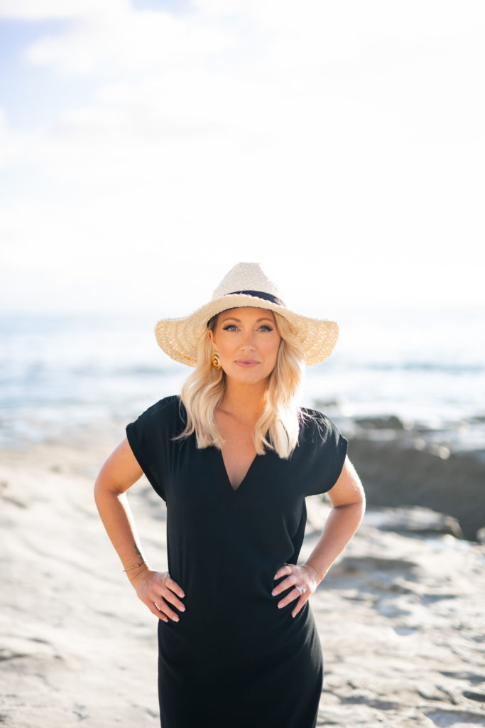 Woman standing at the San Diego beach, wearing a big hat with her hands on her hips.  