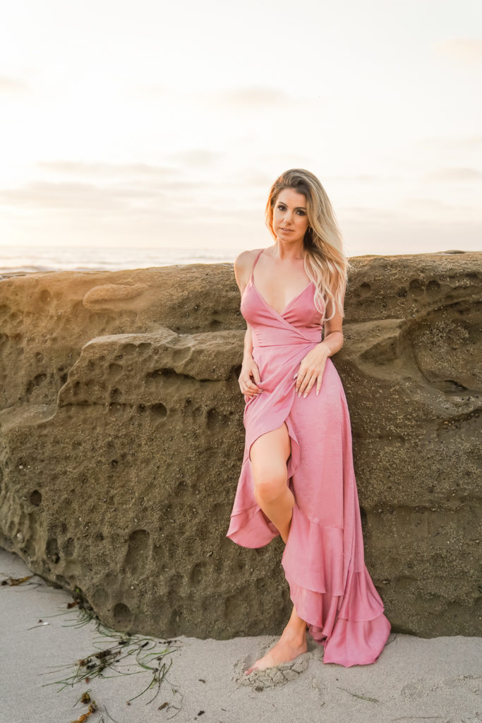 Woman in a pink jumpsuit standing against a rock at the beach