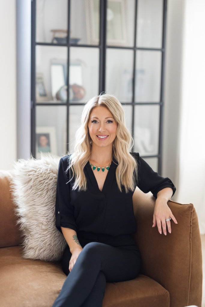 Woman sitting on a brown couch smiling toward the camera during her branding photography session.