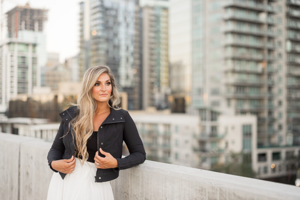 Woman standing in front of downtown San Diego wearing a leather jacket and posing.