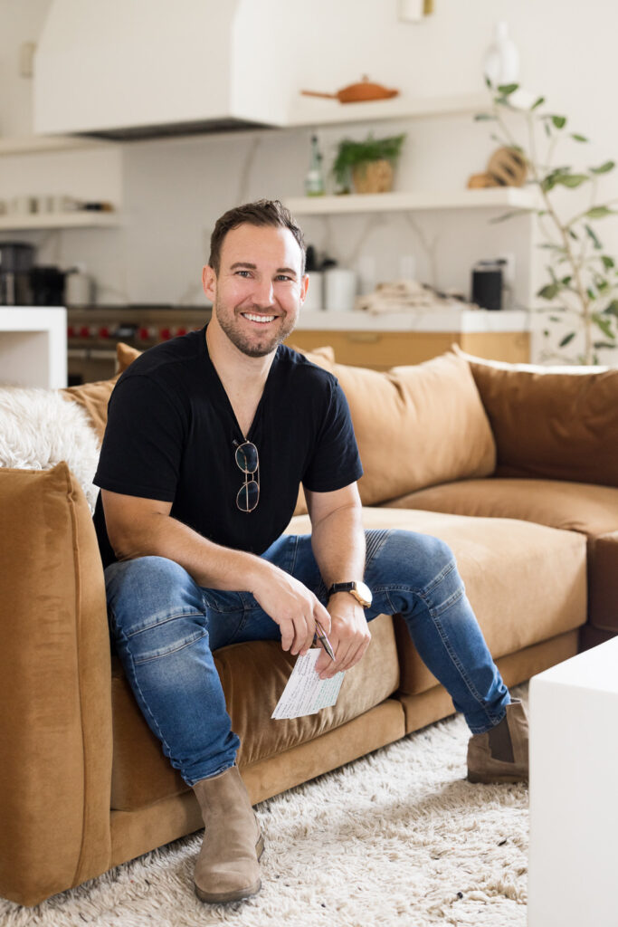 Brand photo of a man sitting on a brown couch and smiling at Meg Marie.