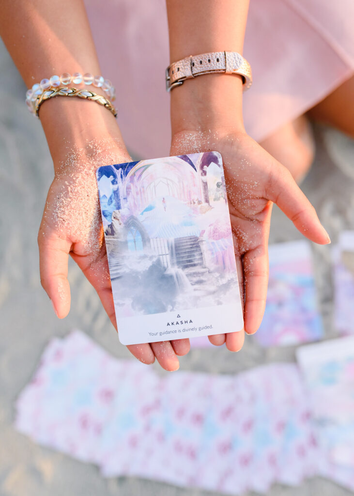 Two hands of a woman holding onto a spiritual healing card at the beach. 