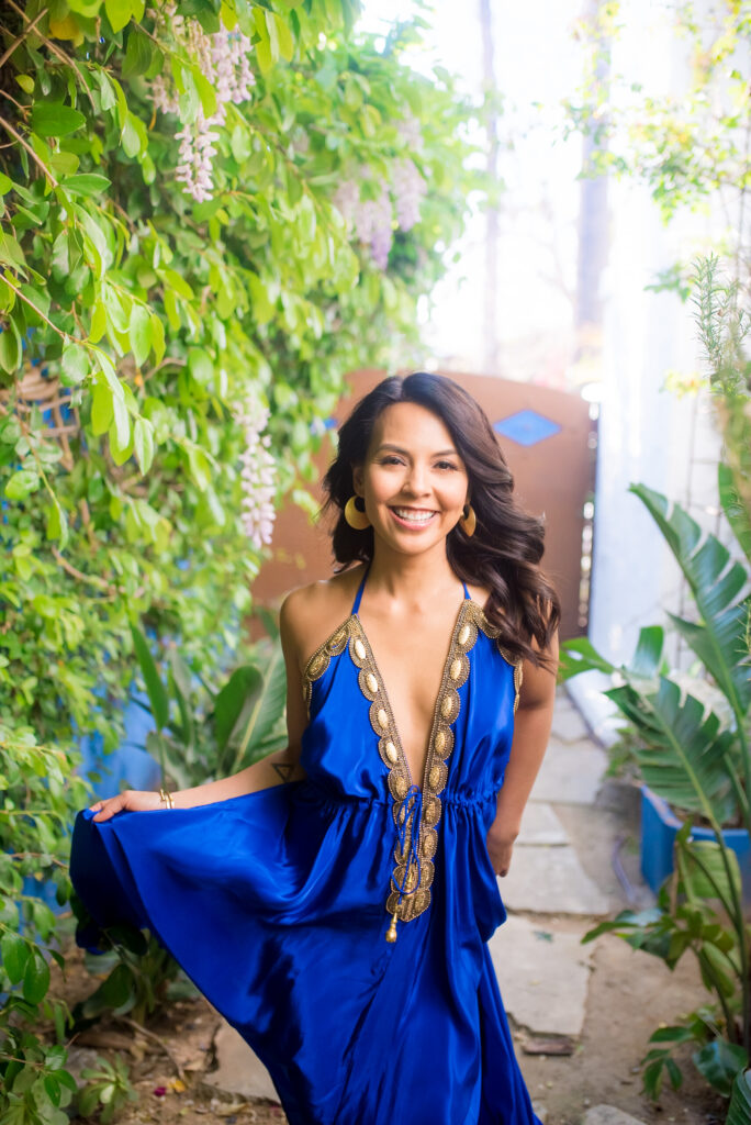 Woman dressed in a blue dress smiling at the camera. 