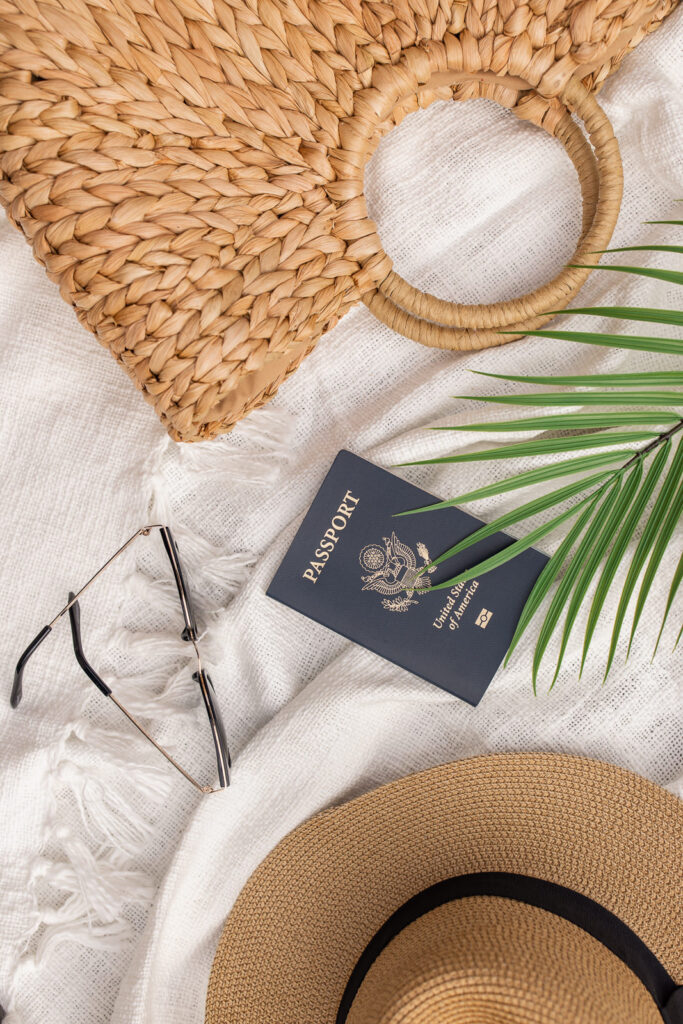 Close-up of a passport, fedora hat, sunglasses, and handbag. 
