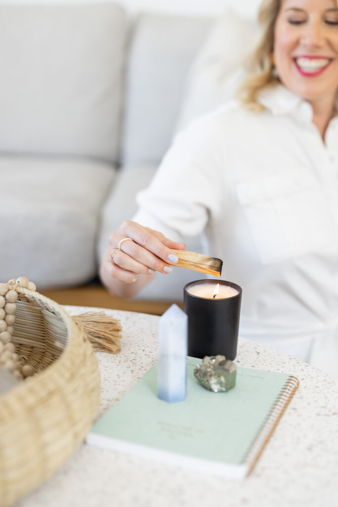 Woman sitting and using a candle to burn Palo Santo with a crystal next to it.