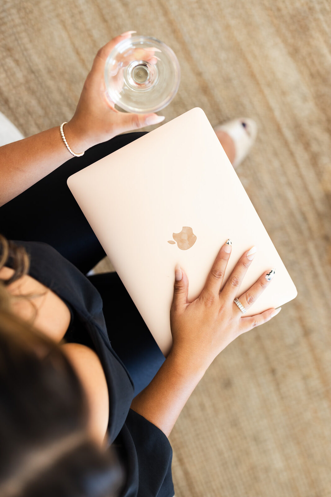 Close-up of a woman’s lap while she's holding a laptop and a glass of wine. 