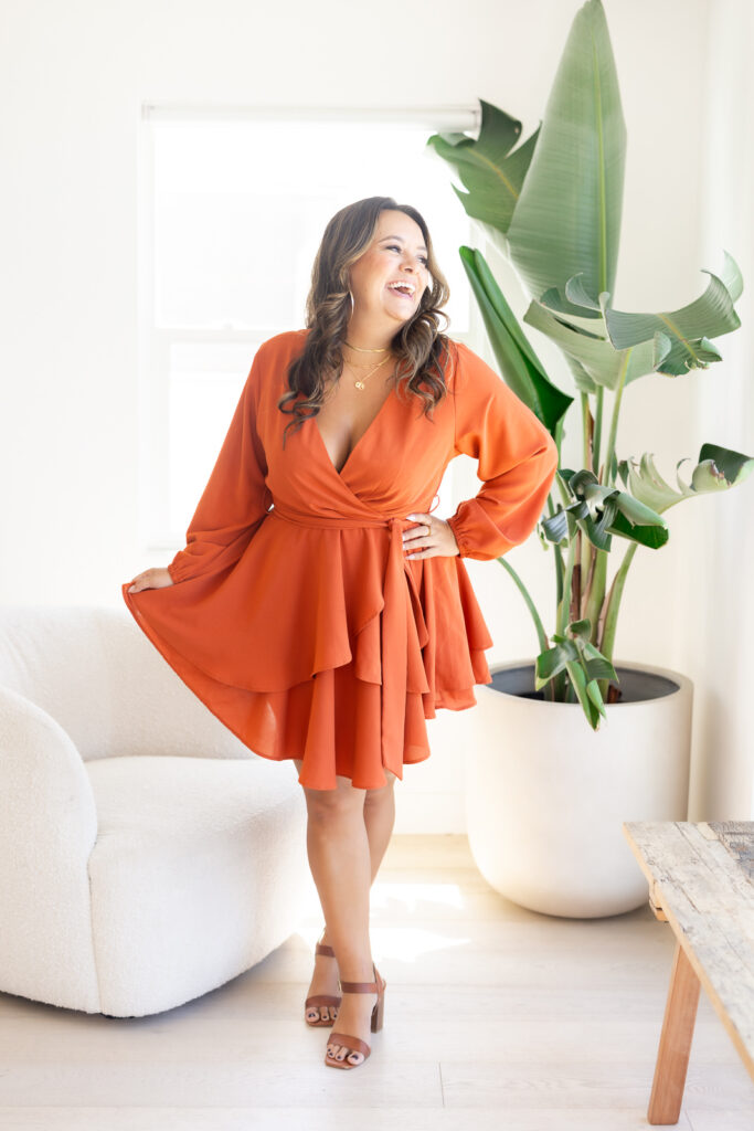 Woman wearing a flowy, orange dress and laughing away from the camera. 
