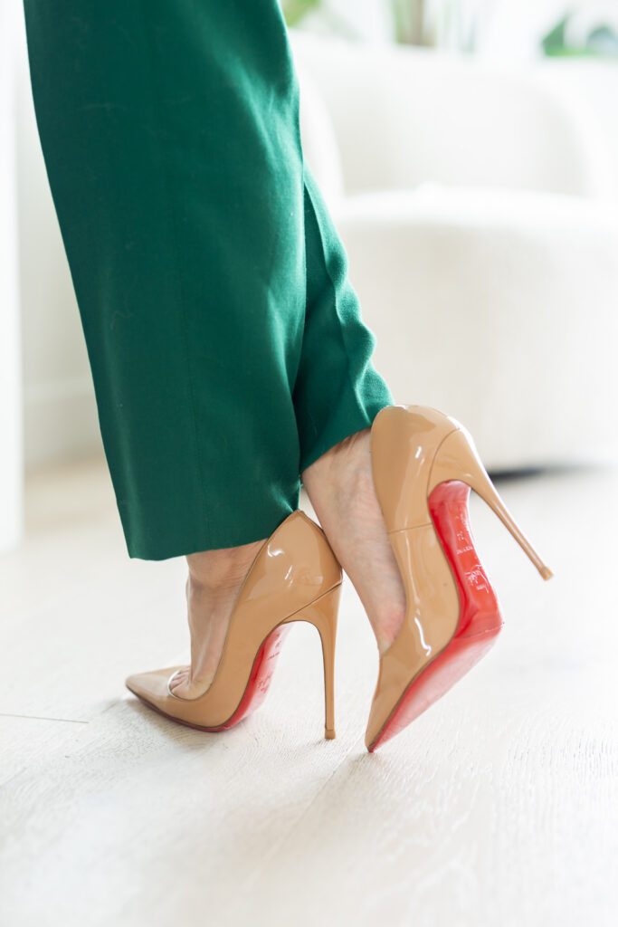Close-up of a woman’s ankles wearing nude-colored heels and green pants. 
