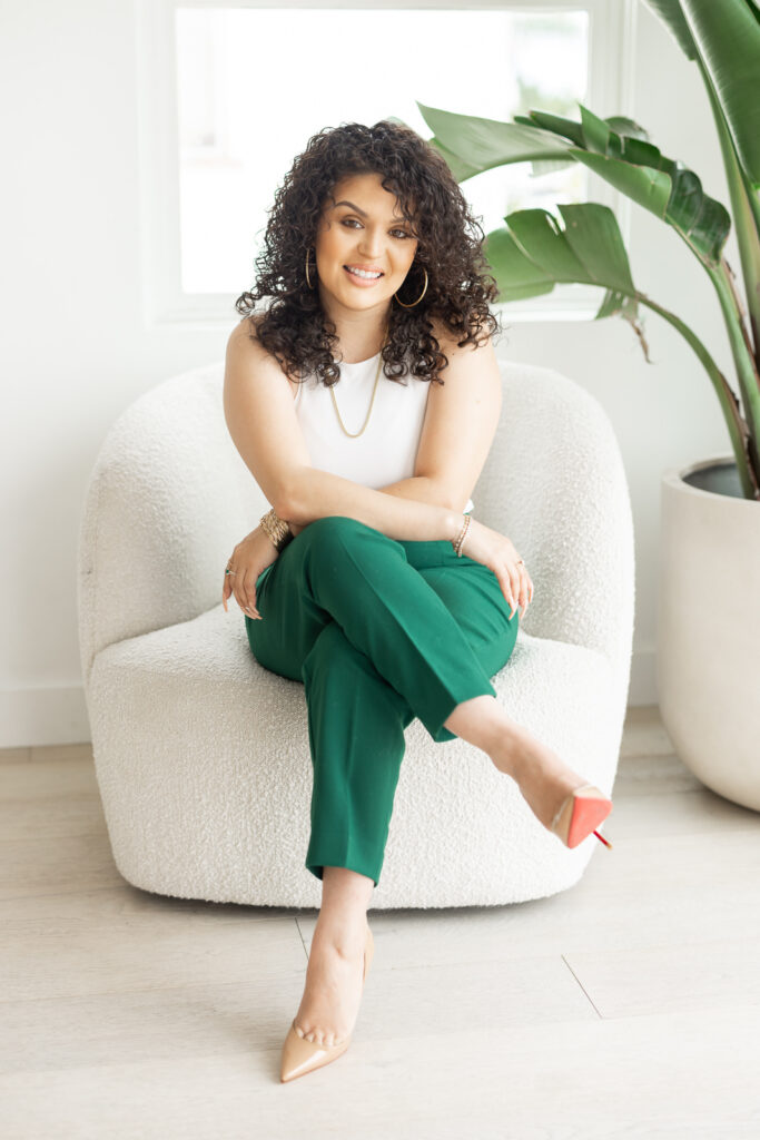 Woman in green pants sitting in a white sofa chair and crossing her legs.

