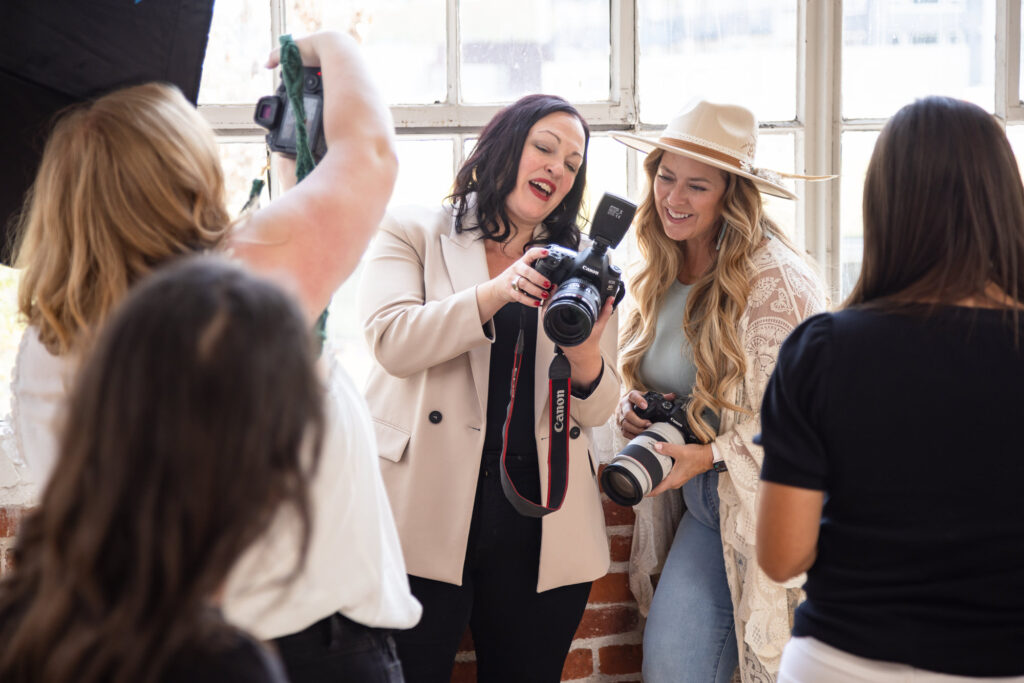 Group of people in a bright room, enjoying photography. Two women smiling and reviewing camera images, creating an upbeat and collaborative atmosphere.
