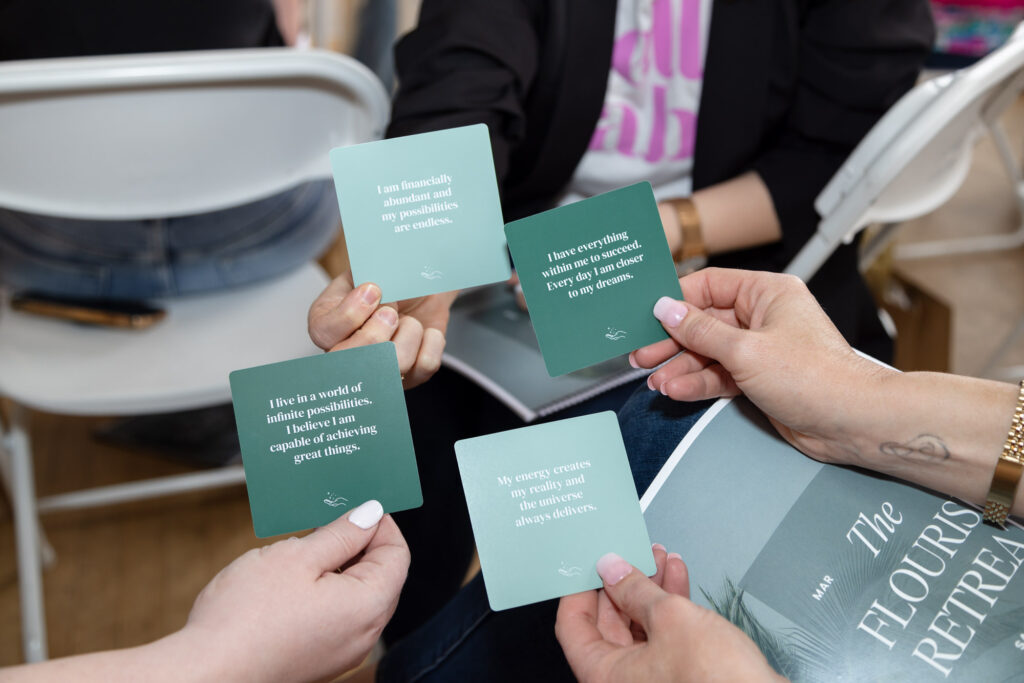 People holding four affirmation cards with positive messages during a retreat. The scene conveys a sense of community, empowerment, and inspiration.