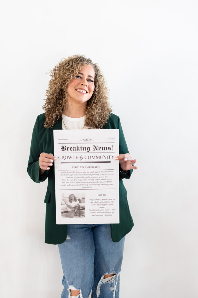 A woman with curly hair smiles while holding a newspaper titled "Breaking News! Growth & Community." She wears a green blazer and ripped jeans against a plain white background. | Meg Marie Photography