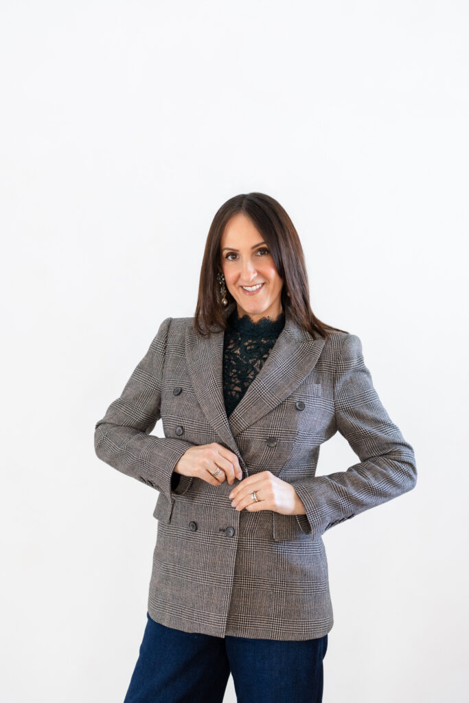 Smiling woman in a gray plaid blazer over a black lace top, with long brown hair, stands against a plain white background, exuding confidence. | Meg Marie Photography